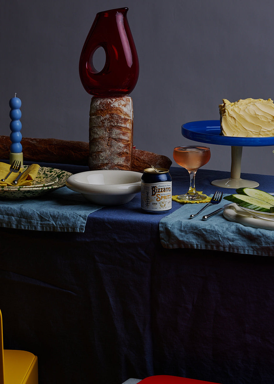 Dining table setup with bread, cake, drinks, and cutlery on a dark background